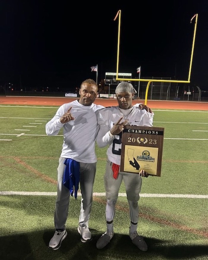 Josiah holding a championship trophy plaque with his dad Lamar by his side
