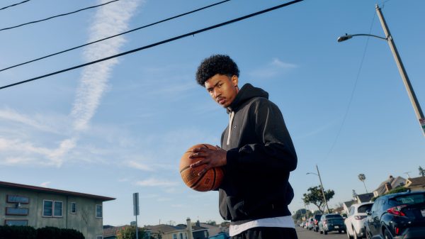 Jason Crowe holds a basketball and stands for a portrait looking down at camera.