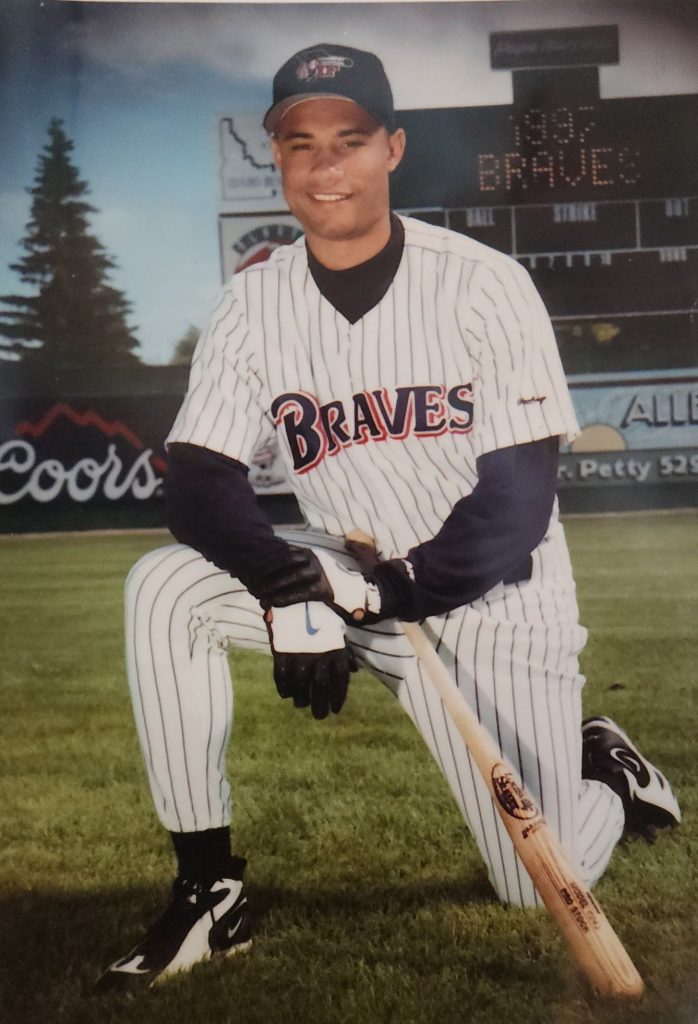 Trajan Langdon wearing a Braves jersey on one knee holding his bat.