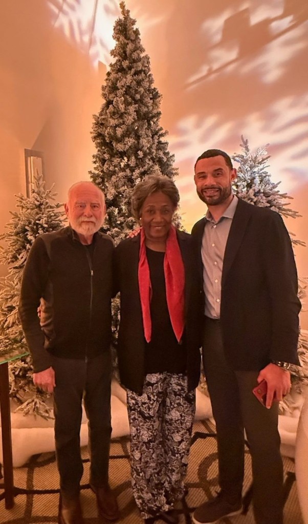 Trajan Langdon poses for a photo with his parents in front of a Christmas tree.