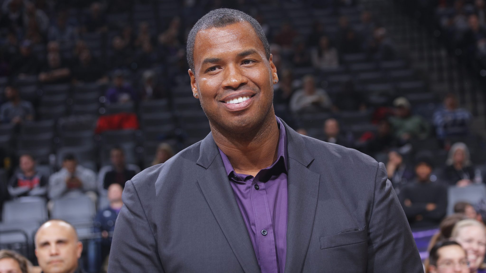 Former NBA player Jason Collins is wearing a suit and smiling.