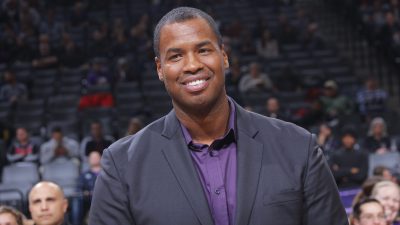 Former NBA player Jason Collins is wearing a suit and smiling.
