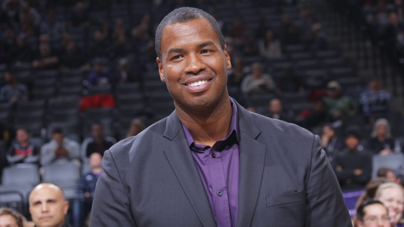 Former NBA player Jason Collins is wearing a suit and smiling.