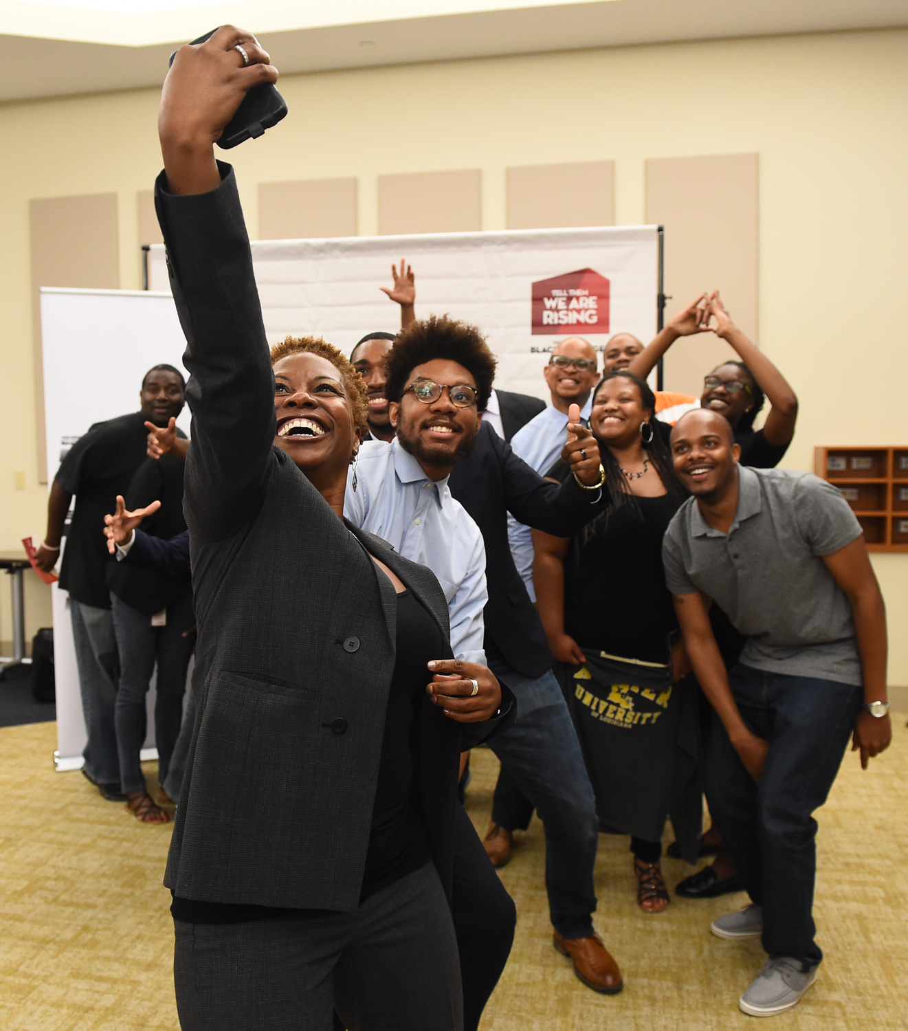 Looking from behind phone as employees take a group selfie.