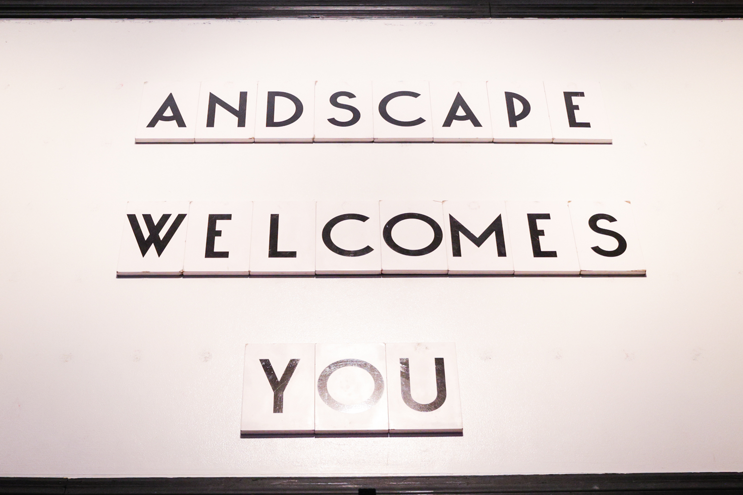 Black letters on white wall spelling "Andscape Welcomes You" with each word it's own row.