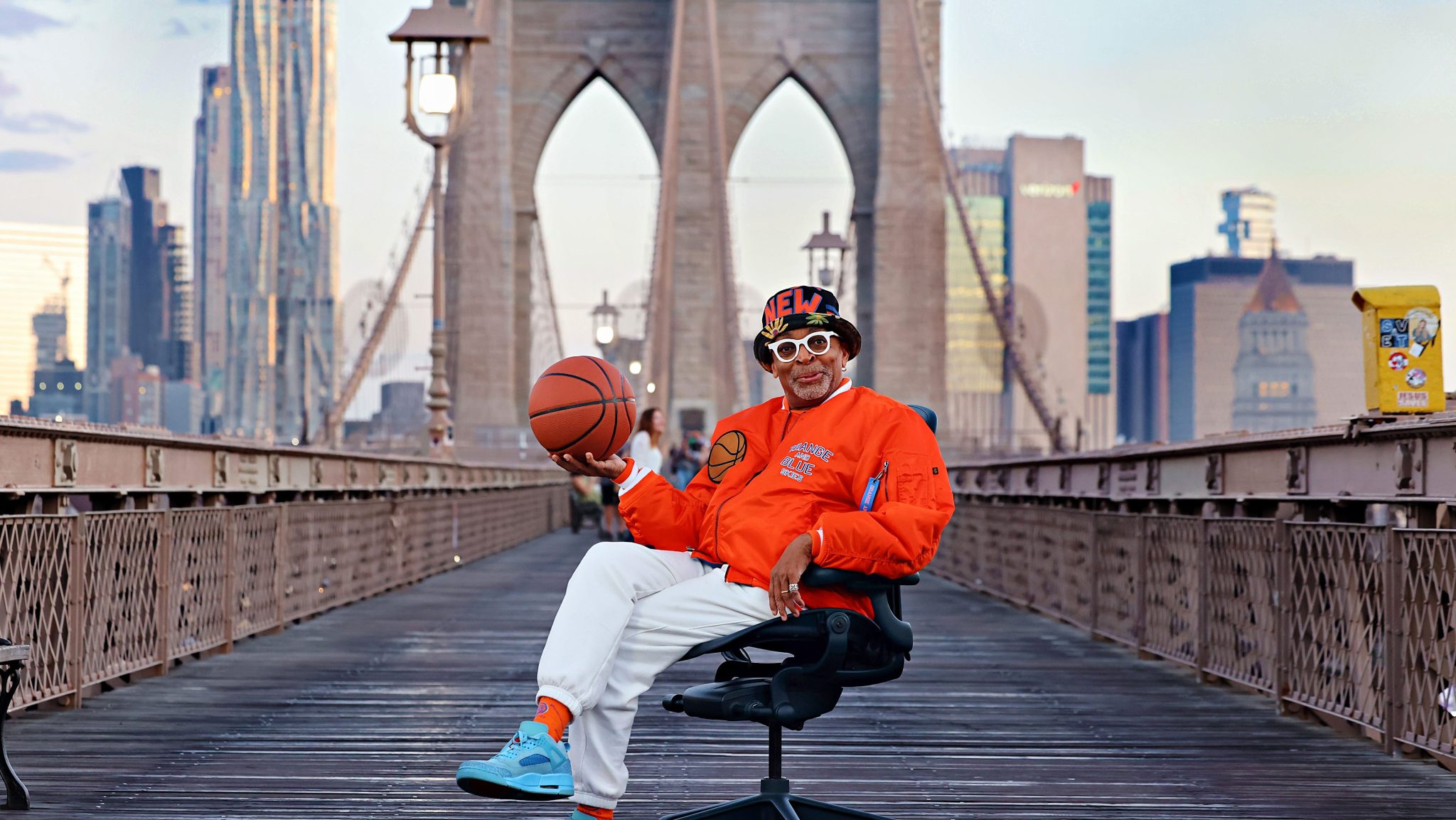 Spike Lee sits in Herman Miller's new nightfall-blue Aeron chair on the Brooklyn Bridge