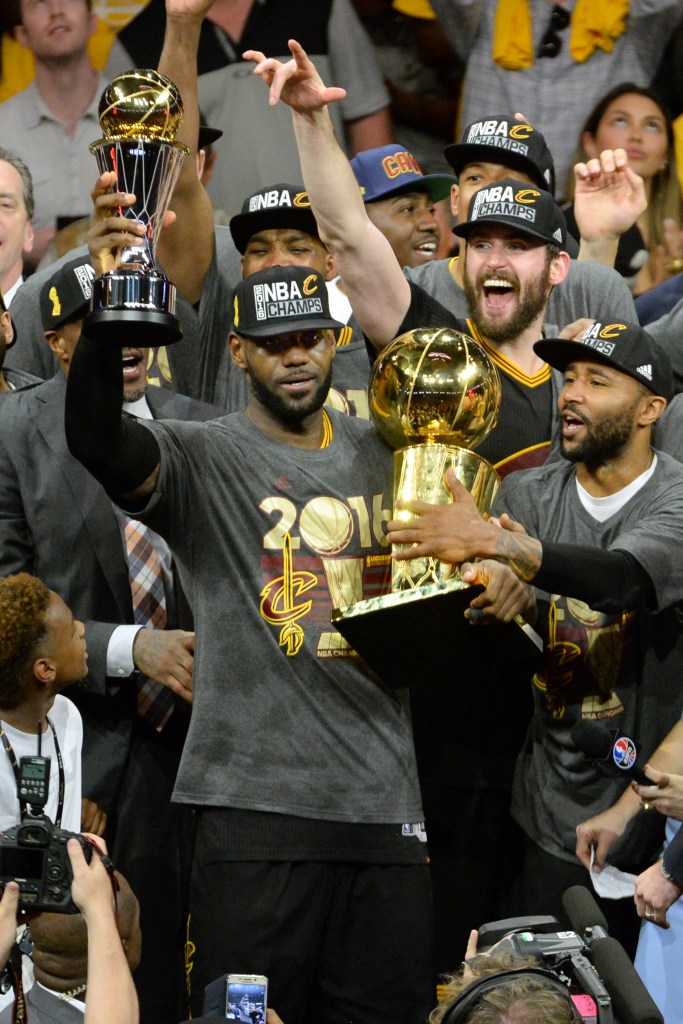 LeBron James holds the NBA championship trophy as teammates surround him.