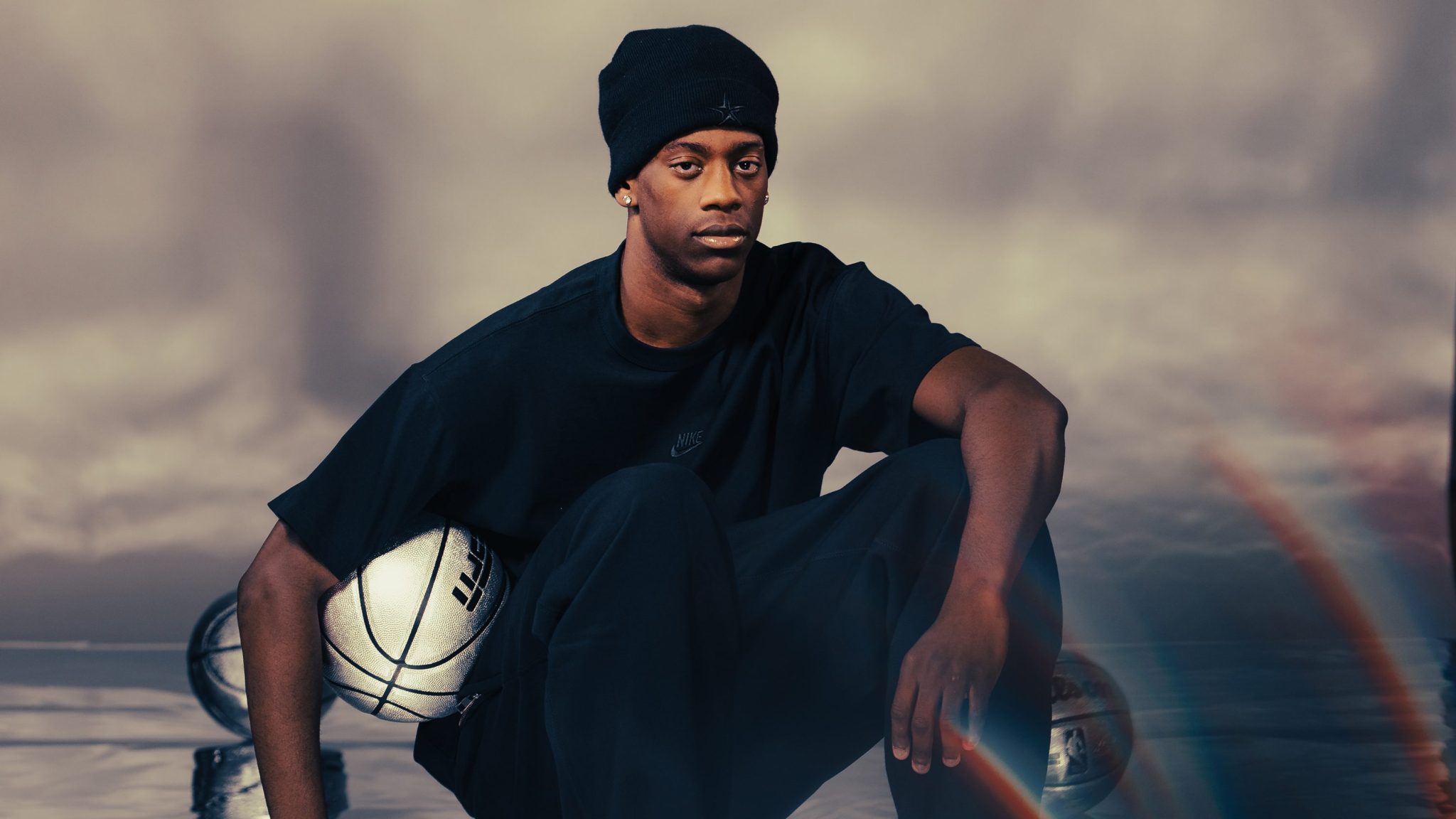 AJ Dybantsa holds a silver basketball player with an ESPN logo in front of a grey cloudy backdrop with a rainbow in the bottom right corner.