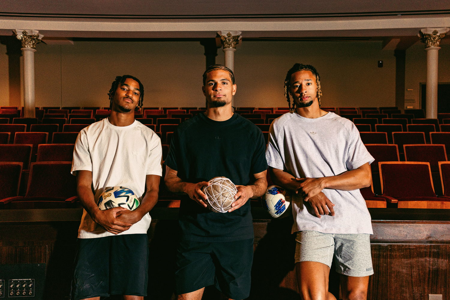 From left: Kenji Mboma Dem, Miles Robinson and Ayoub Jabbari pose for a photo in Music Hall in Cincinnati. Robinson holds a ball made of plastic bags and string, while Mboma Den and Jabbari pose with traditional soccer balls.