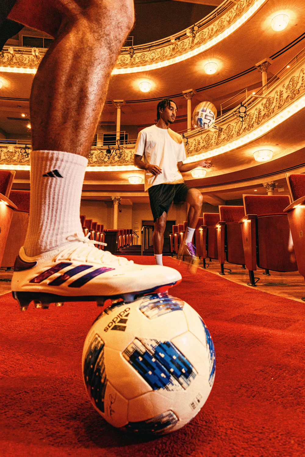 Miles Robinson (left) rests his foot on a soccer ball while Kenji Mboma Dem dribbles a ball in the background inside Music Hall in Cincinnati. 