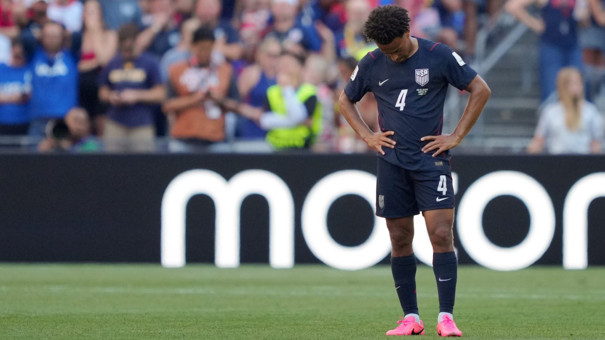 Tyler Adams has his hands on his hips and looks down as he stands on the field.